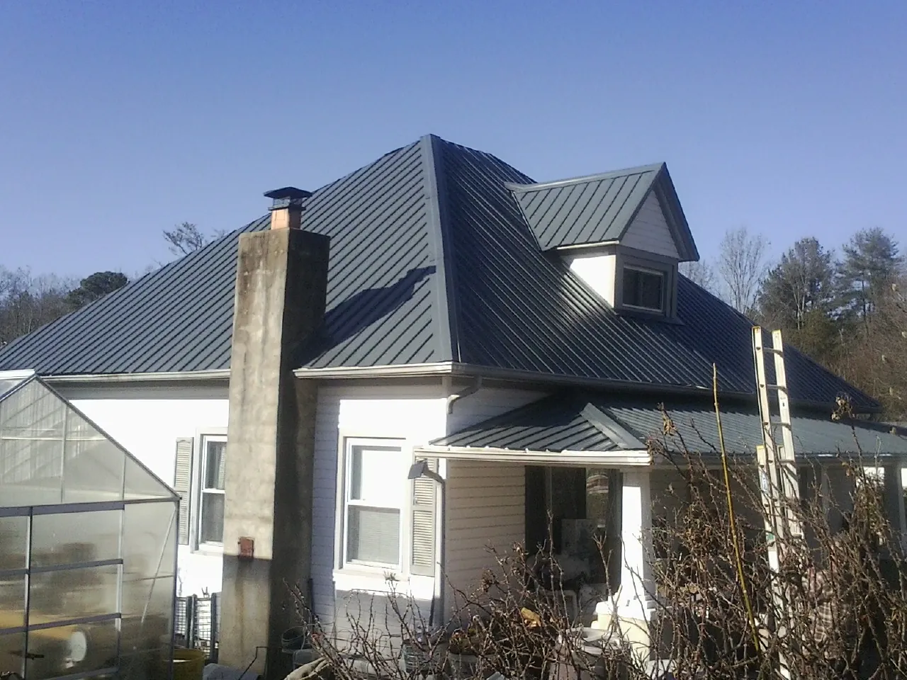 Dark blue standing seam metal roof on a white farmhouse with dormer — Slate & Tile Roof Repair by Roofing Brothers in Potomac