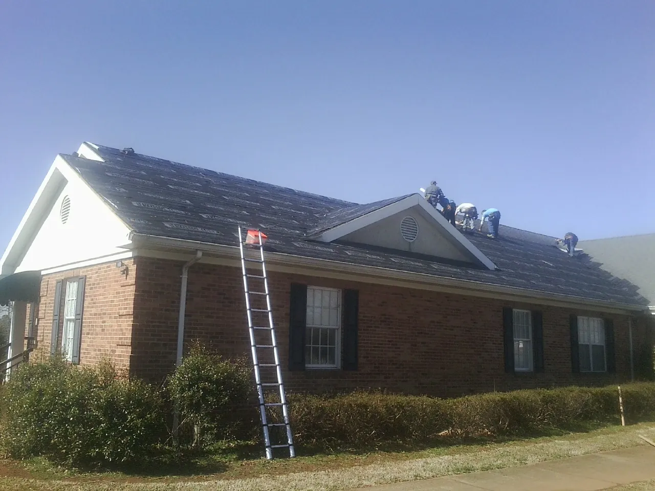 Crew tearing shingles off a brick ranch roof with a ladder set — Emergency Roof Repair work by our crew in Potomac