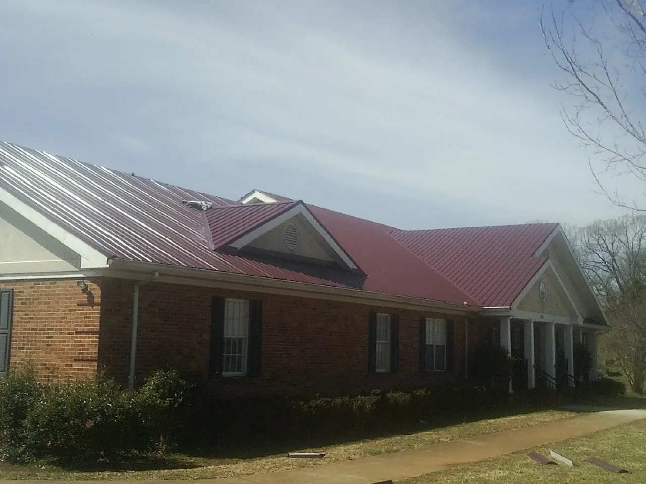 Red metal roof with gabled entries on a long brick building, from a Hail Damage Roof Repair job in Potomac