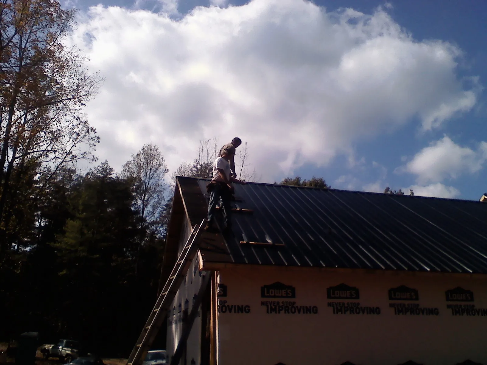 Roofer fastening dark metal panels high against a cloudy sky, from a Roof Inspection job in Potomac
